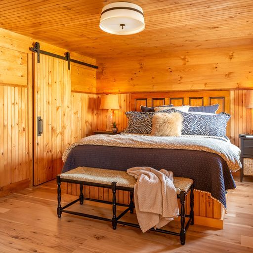 Custom-built bed with a reclaimed five-panel door headboard and built-in storage drawers underneath at Camp Ridlon